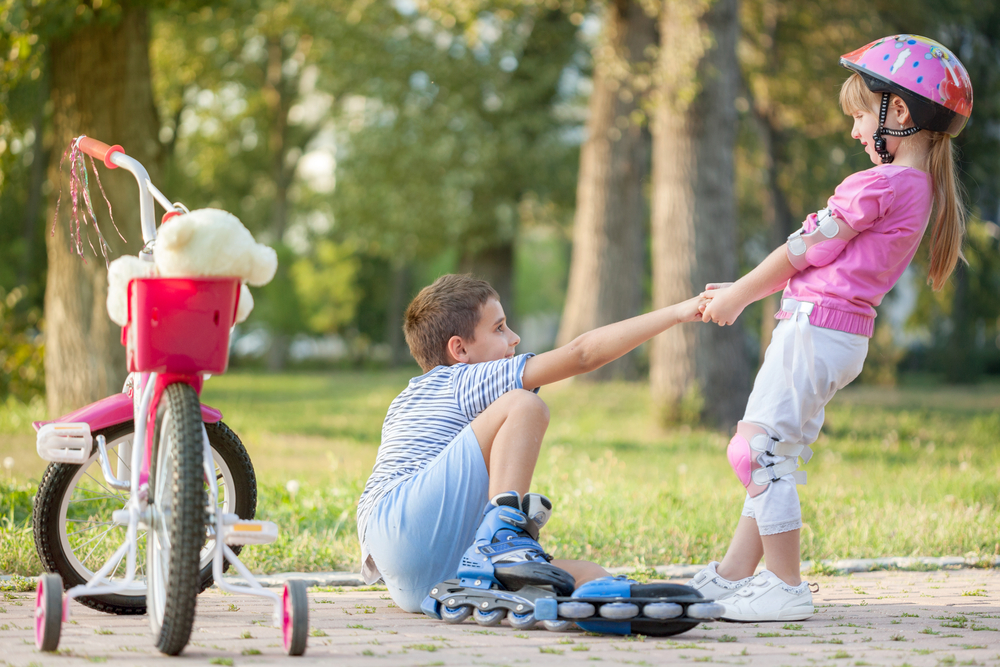 A girl helping a boy up after he fell roller blading.